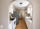 Arched entry to the kitchen featuring wood-finish flooring, white cabinetry, a double basin stainless steel sink, and a multi-tone tile backsplash - 10439 36A Ave Nw, Edmonton, AB 
