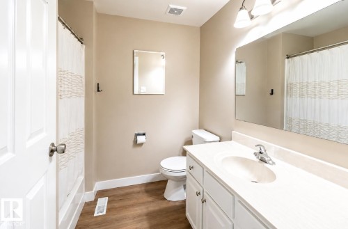 Wood-finish flooring, white vanity with integrated sink, chrome faucet, wall-mounted mirror, and overhead vanity lighting - 10439 36A Ave Nw, Edmonton, AB 