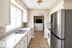 Kitchen featuring white cabinetry, a double basin stainless steel sink, tile backsplash, and stainless steel refrigerator - 