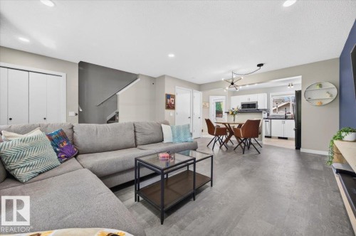 Open-concept living area with plank-style flooring, recessed lighting, and a modern kitchen featuring white cabinetry and stainless steel appliances - 1217 76 Street Sw, Edmonton, AB 