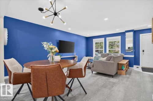 Recessed lighting, wood-finish flooring, two large windows with white trim, a modern Sputnik chandelier, and a white front entry door - 1217 76 Street Sw, Edmonton, AB 