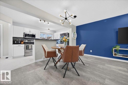Eat-in kitchen featuring stainless steel appliances, white cabinetry, a black countertop, and a tile backsplash - 1217 76 Street Sw, Edmonton, AB 