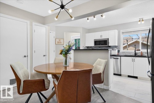 Kitchen with white cabinetry, stainless steel appliances, dark countertops, and a tiled backsplash - 1217 76 Street Sw, Edmonton, AB 