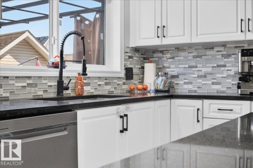 White shaker-style cabinetry with matte black hardware, dark countertops, mosaic tile backsplash, stainless steel dishwasher, and a gooseneck faucet - 1217 76 Street Sw, Edmonton, AB 