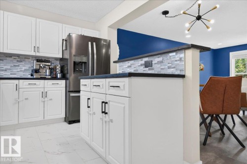 White shaker cabinetry with dark hardware, stainless steel refrigerator, tile backsplash, dark countertops, and light tile flooring - 1217 76 Street Sw, Edmonton, AB 