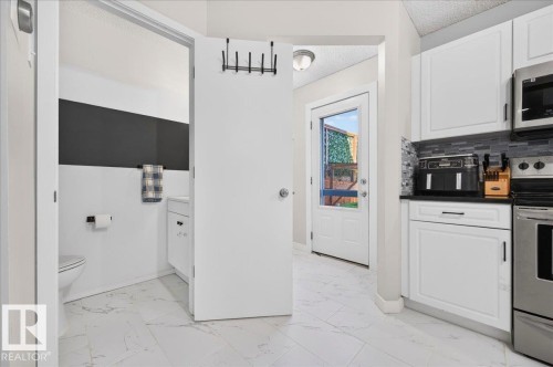 Kitchen with white cabinetry, dark countertops, tile backsplash, and stainless steel appliances - 1217 76 Street Sw, Edmonton, AB 
