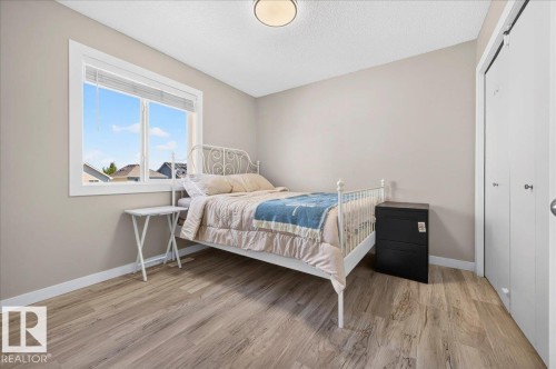 Wood-finish flooring, neutral wall tones, white trim, a large window, and white bi-fold closet doors - 1217 76 Street Sw, Edmonton, AB 
