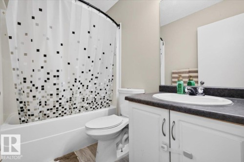 Bathroom featuring a tub/shower combination, white toilet, vanity with an integrated sink, dark countertop, and wood-finish flooring - 1217 76 Street Sw, Edmonton, AB 