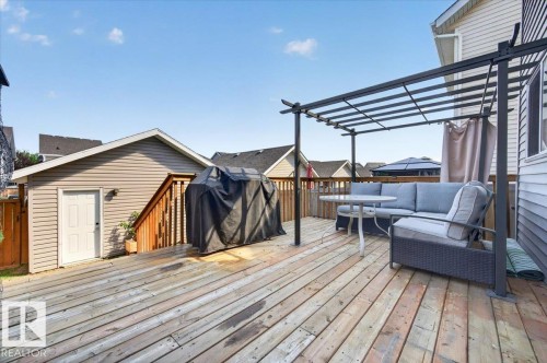 Expansive wood deck with a metal pergola, privacy curtain, and adjacent exterior building with siding and a side entrance - 1217 76 Street Sw, Edmonton, AB 