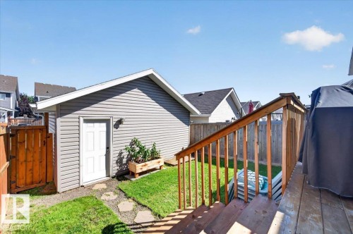 Detached outbuilding with horizontal siding, a private wood fence, a grassy yard, stone pathway, and wood deck with stairs - 1217 76 Street Sw, Edmonton, AB 