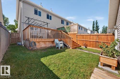 Expansive backyard featuring a wood deck with pergola, wood privacy fencing, a raised garden bed, and a grass lawn - 1217 76 Street Sw, Edmonton, AB 