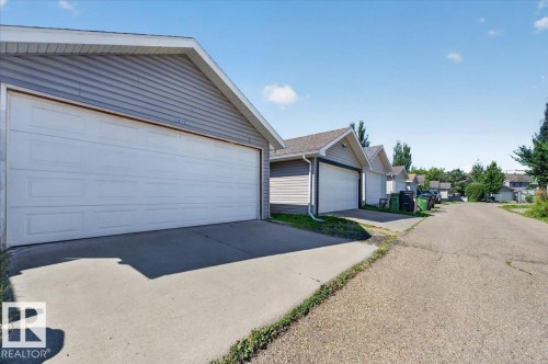 Attached garage with panel door, vinyl siding exterior, and concrete driveway - 1217 76 Street Sw, Edmonton, AB 