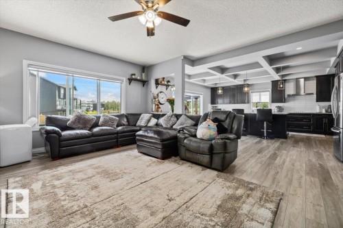 Open-concept living area featuring wood-finish flooring, a contemporary ceiling fan, and large windows - 5203 23A Avenue Sw, Edmonton, AB - Indoor Photo Showing Living Room