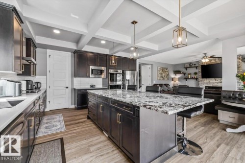 Gourmet kitchen featuring dark wood cabinetry, stainless steel appliances, a large central island with seating, granite countertops, and wood-finish flooring - 5203 23A Avenue Sw, Edmonton, AB - Indoor Photo Showing Kitchen With Upgraded Kitchen