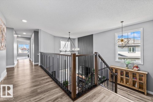 Staircase with dark wood newel posts and metal balusters, featuring wood-finish flooring and grey wall paint - 5203 23A Avenue Sw, Edmonton, AB - Indoor Photo Showing Other Room