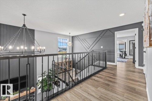 Upper-level hallway featuring wood-finish flooring, a contemporary black metal railing, and accent walls with geometric paneling and vertical slats - 5203 23A Avenue Sw, Edmonton, AB - Indoor Photo Showing Other Room