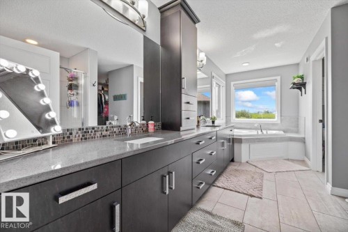 Spacious bathroom featuring an integrated soaking tub, dual vanity with quartz countertop, extensive built-in cabinetry, and tile flooring - 5203 23A Avenue Sw, Edmonton, AB - Indoor Photo Showing Bathroom