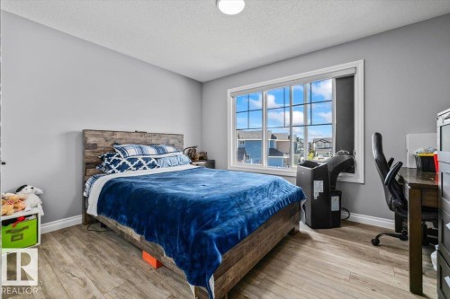 Spacious room featuring light gray walls, wood-finish flooring, a large window with white trim, and a built-in desk area - 5203 23A Avenue Sw, Edmonton, AB - Indoor Photo Showing Bedroom