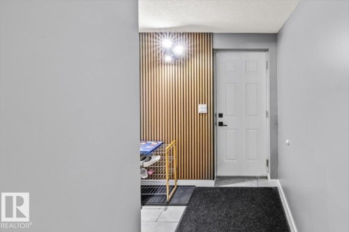Entryway featuring a wood-panel accent wall, modern flush-mount lighting, a white panel door with black hardware, and light-toned floor tiling - 5203 23A Avenue Sw, Edmonton, AB - Indoor Photo Showing Other Room