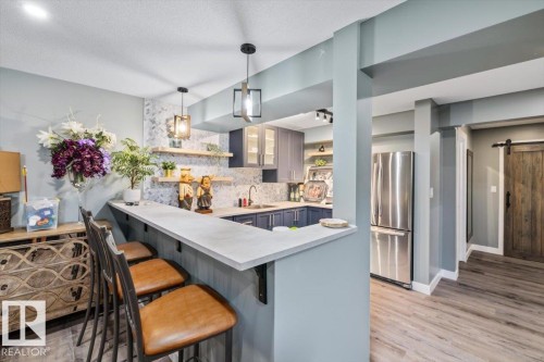 Kitchenette with a breakfast bar, featuring light wood-finish flooring and a stainless steel refrigerator - 5203 23A Avenue Sw, Edmonton, AB - Indoor Photo Showing Kitchen With Upgraded Kitchen