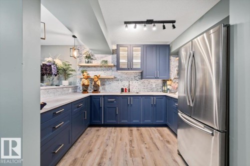 Kitchenette featuring navy blue cabinetry with brushed nickel hardware, light-toned countertops, a full-size stainless steel refrigerator, wood-finish flooring, and track lighting - 5203 23A Avenue Sw, Edmonton, AB - Indoor Photo Showing Kitchen With Upgraded Kitchen