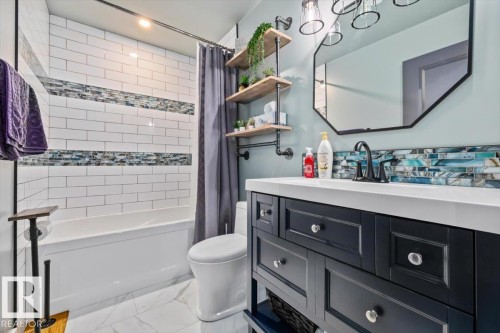 Contemporary bathroom featuring a dark vanity with a white countertop and a geometric mirror - 5203 23A Avenue Sw, Edmonton, AB - Indoor Photo Showing Bathroom