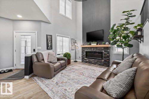 Living area featuring a floor-to-ceiling accent wall with vertical slat paneling, an integrated electric fireplace with a stone surround, and wood-finish flooring - 5203 23A Avenue Sw, Edmonton, AB - Indoor Photo Showing Living Room With Fireplace
