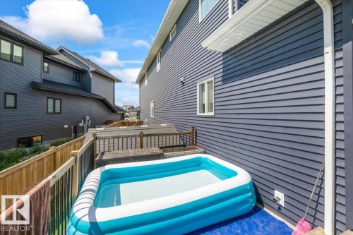 Side yard featuring a multi-level deck with dark wood railings, wood privacy fencing, and blue vinyl siding on the exterior - 5203 23A Avenue Sw, Edmonton, AB - Outdoor With Exterior