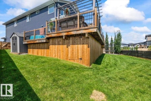 Expansive backyard featuring a manicured lawn, a raised wooden deck with black railings and a pergola, and a wooden fence - 5203 23A Avenue Sw, Edmonton, AB - Outdoor