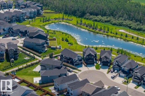 Aerial perspective showcasing a residential development with individual properties, a central cul-de-sac, and a prominent natural water feature bordered by lush greenery and dense tree cover - 5203 23A Avenue Sw, Edmonton, AB - Outdoor With Body Of Water With View
