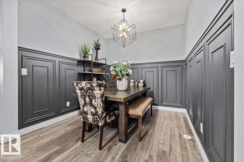 Room featuring wood-finish flooring, dark wainscoting, and a modern geometric light fixture - 5203 23A Avenue Sw, Edmonton, AB - Indoor Photo Showing Dining Room
