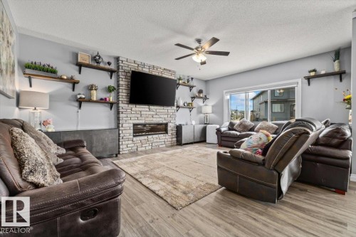 Living area featuring wood-finish flooring and a stone-clad fireplace with an integrated linear firebox - 5203 23A Avenue Sw, Edmonton, AB - Indoor Photo Showing Living Room With Fireplace