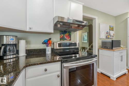 Stainless steel appliance suite with a range and coordinating hood, white cabinetry, dark granite countertops, and maple hardwood flooring - 10531 137 Street Nw, Edmonton, AB 