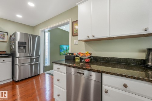 Stainless steel French door refrigerator, white cabinetry, granite countertops, stainless steel dishwasher, and maple hardwood flooring - 10531 137 Street Nw, Edmonton, AB 