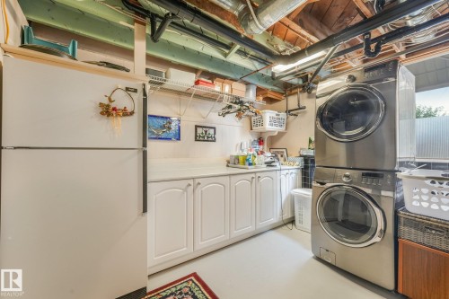 Bright Laundry area featuring a stacked washer and dryer, white cabinetry with a countertop, and a full-size refrigerator - 10531 137 Street Nw, Edmonton, AB 