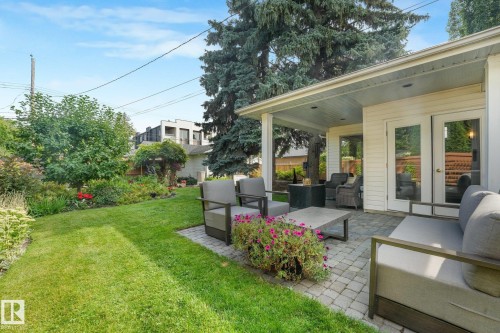 Expansive backyard featuring a covered patio, paved stone hardscaping, lush green lawn, and mature landscaping - 10531 137 Street Nw, Edmonton, AB 