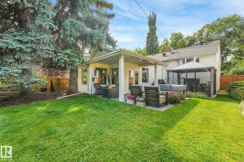 Spacious backyard retreat featuring a manicured lawn, mature evergreen and deciduous trees, and a modern covered patio with white columns - 10531 137 Street Nw, Edmonton, AB 