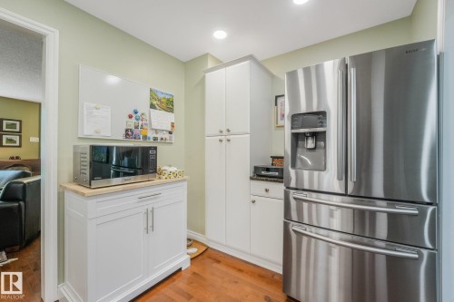 Stainless steel French door refrigerator, white shaker-style cabinetry, maple hardwood floors, recessed lighting, and granite countertops. - 10531 137 Street Nw, Edmonton, AB 
