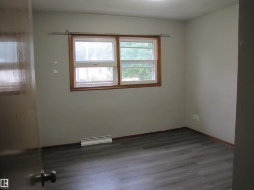 Wood-finish flooring with perimeter baseboards, light-toned walls, and a multi-pane window with wood trim - 9512 63 Avenue Nw, Edmonton, AB 