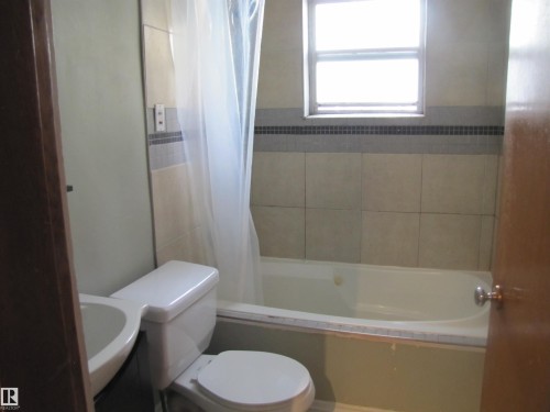 Tiled shower and bath surround featuring a decorative tile accent band and a window - 9512 63 Avenue Nw, Edmonton, AB 