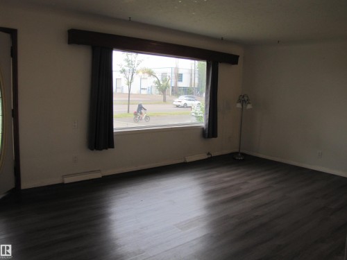 Spacious room with dark wood-finish flooring, a large picture window, and white walls - 9512 63 Avenue Nw, Edmonton, AB 