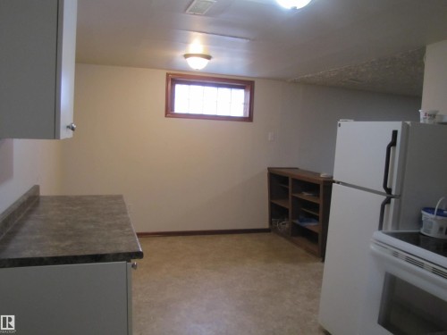 Galley kitchen featuring white cabinetry, a laminate countertop, and vinyl flooring - 9512 63 Avenue Nw, Edmonton, AB 