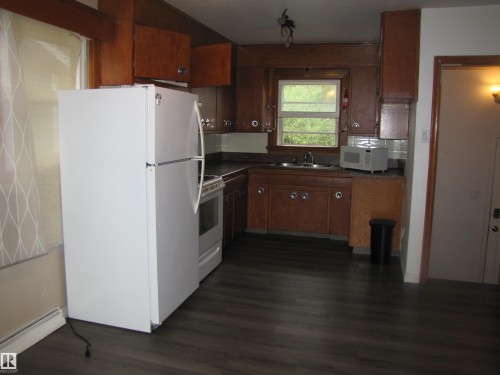 Kitchen featuring wood-finish flooring, dark countertops, wood cabinetry, and a window above the sink - 9512 63 Avenue Nw, Edmonton, AB 