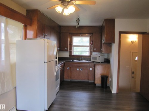 Kitchen featuring wood-finish cabinetry, dark countertops, a window, and wood-finish flooring - 9512 63 Avenue Nw, Edmonton, AB 