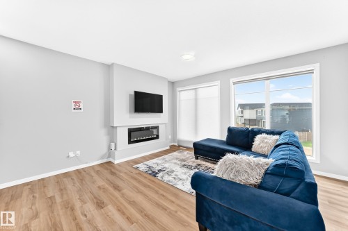 Living space featuring wood-finish flooring, a built-in electric fireplace, and large windows with roller shades - 479 39 St Sw, Edmonton, AB 