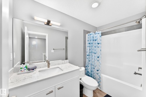 Vanity with a white countertop and integrated sink, brushed nickel faucet, large wall mirror, and integrated bath/shower unit - 479 39 St Sw, Edmonton, AB 