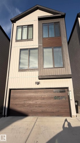 Contemporary exterior featuring vertical siding, mixed material facade, dark-framed windows, and a wood-finish garage door with decorative inserts - 479 39 St Sw, Edmonton, AB 
