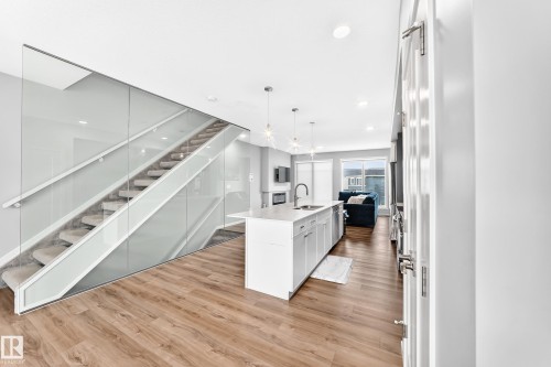 Wood-finish flooring throughout, contemporary glass staircase with carpeted treads, white kitchen island with undermount sink, built-in stainless steel dishwasher, and recessed lighting - 479 39 St Sw, Edmonton, AB 