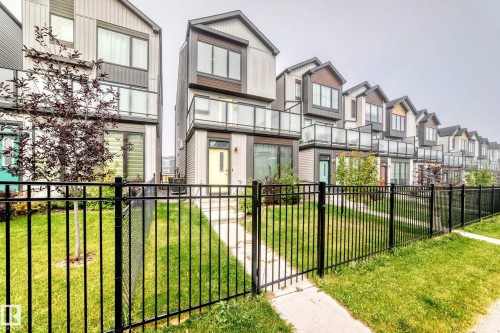 Modern townhome exterior featuring contemporary siding, upper-level balconies with glass railings, and a fenced front yard with a walkway - 479 39 St Sw, Edmonton, AB 