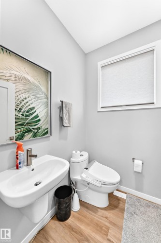 Pedestal sink with a single-hole faucet, modern toilet, and wood-finish flooring - 479 39 St Sw, Edmonton, AB 